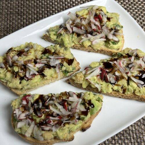 A slice of toast topped with mashed avocado and chickpeas, garnished with herbs