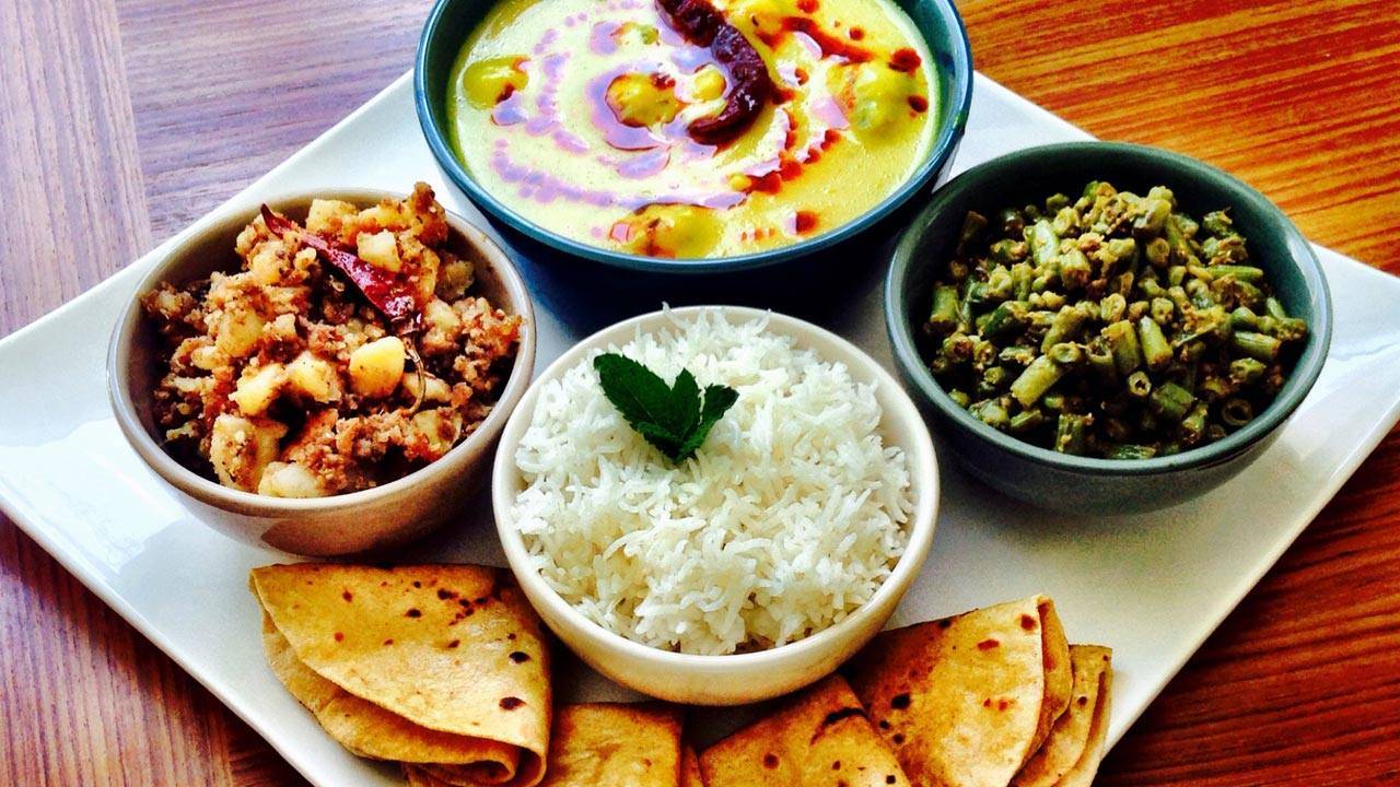 A colorful and appetizing Indian meal featuring bowls of rice, potato curry, green beans, and kadhi, accompanied by fresh chapatis.