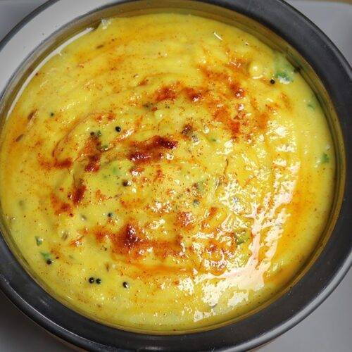 A bowl of creamy yellow Pithla, garnished with chopped fresh cilantro, served alongside traditional Indian accompaniments on a textured surface.