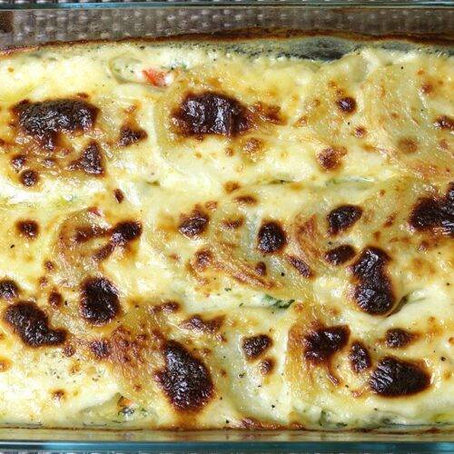 A glass baking dish filled with golden brown scalloped potatoes topped with a creamy, bubbly cheese sauce.