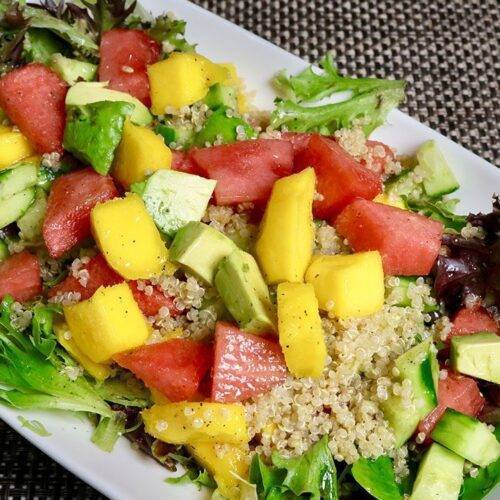 A vibrant and colorful Spring Quinoa Fruit Salad featuring mixed greens, quinoa, watermelon, mango, cucumber, and avocado.